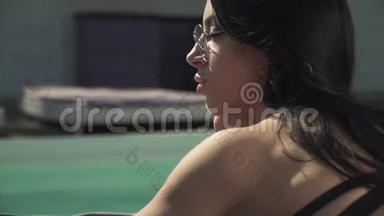躺在游泳池附近的成人时尚女士的肖像。 穿比基尼和太阳镜的可爱女士休闲
